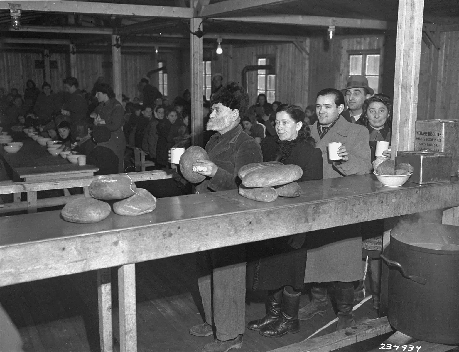 Jewish displaced persons holding bread and mugs as they queue for rations in a wooden hall at a camp in Linz, Austria