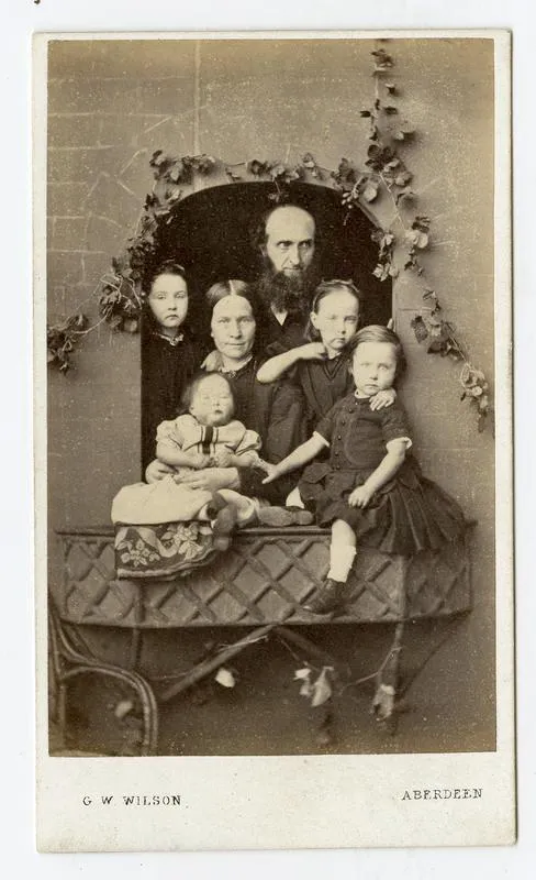 A Victorian carte de visite of a bearded father, a mother and five young children posed together at a mock window decorated with ivy