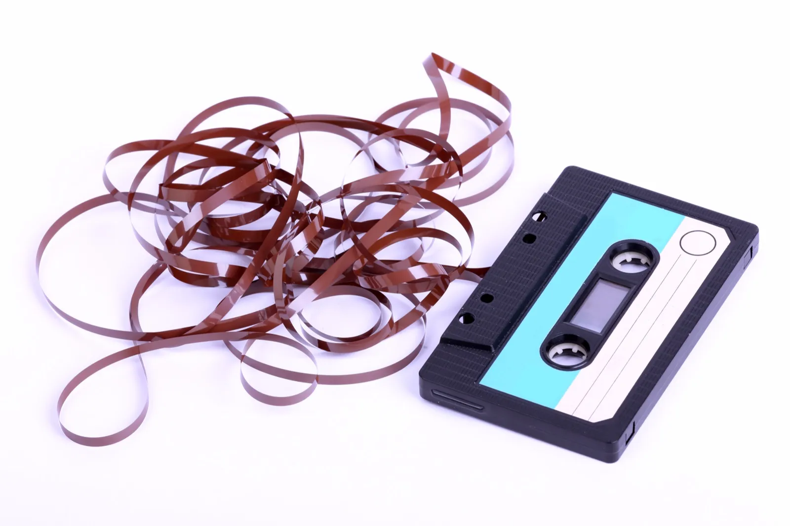 A black audio cassette lying beside a tangle of brown magnetic tape pulled out of it