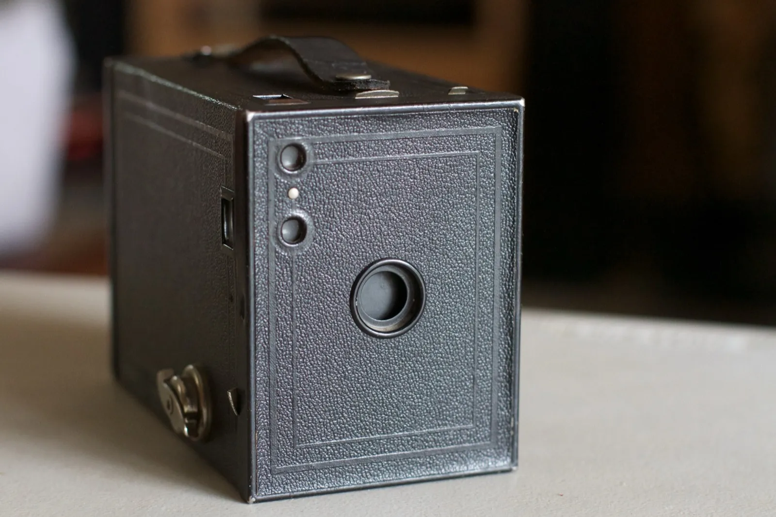A black Kodak Brownie box camera with a leather carrying strap, standing on a table