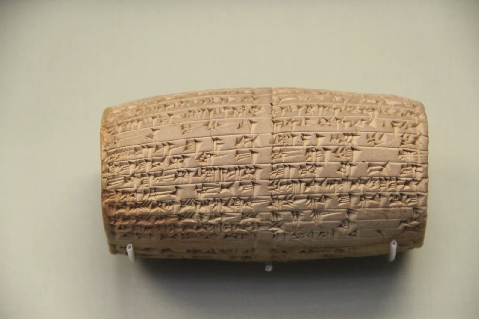 A clay cylinder covered in neat rows of cuneiform script, displayed in a museum case