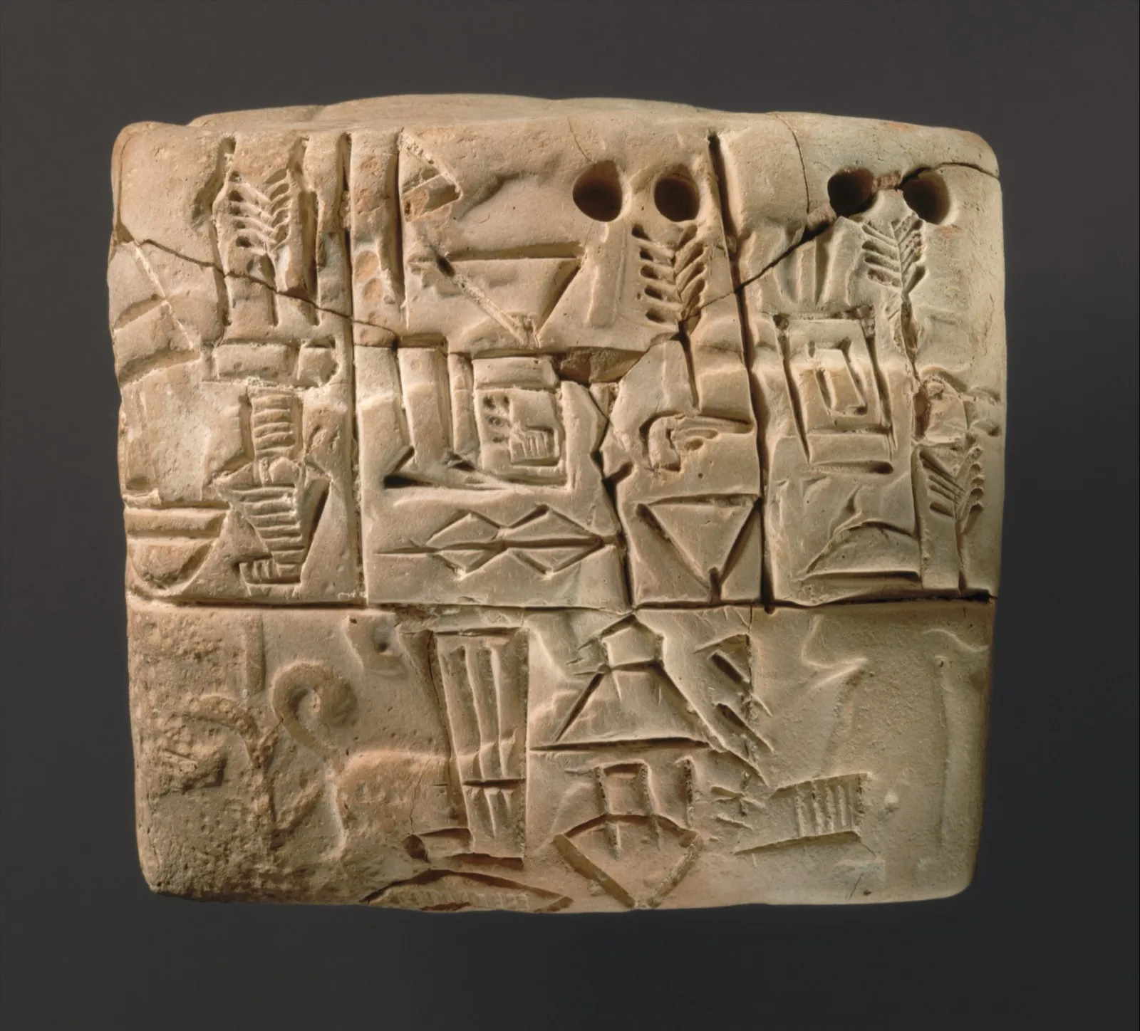 A small clay tablet from Mesopotamia covered in pressed numerals and carved signs, including ears of barley