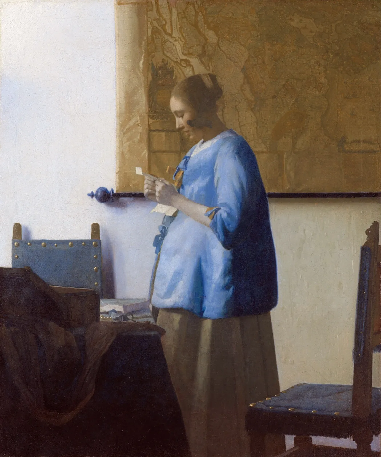 A young woman in a blue jacket standing by a window, intently reading a letter, with a map on the wall behind her