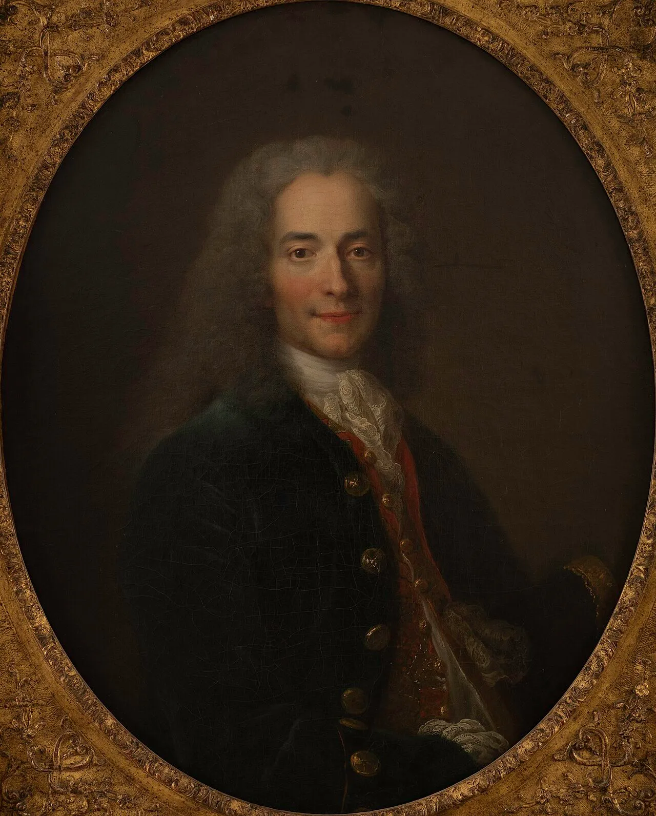 A portrait of Voltaire as a young man, with long curled grey wig, dark coat and lace cravat, in an oval gilt frame