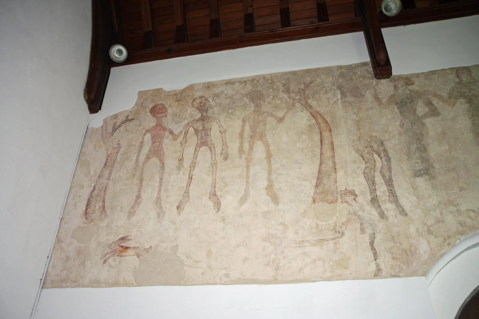 A fourteenth-century wall painting of three skeletal figures beside a tree, in a whitewashed English church